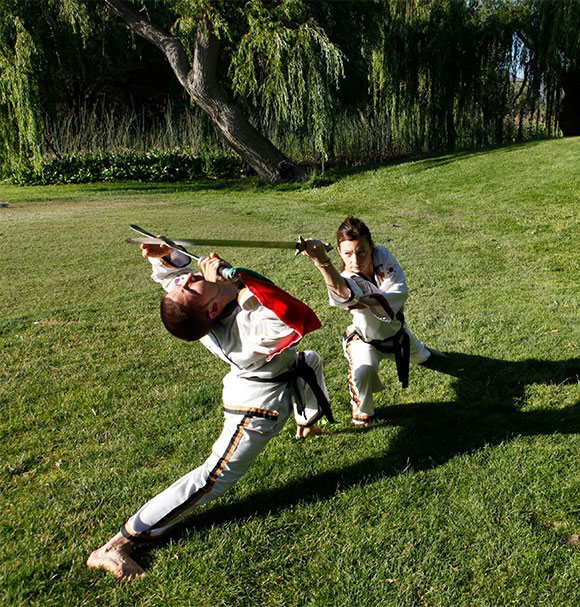 Two people combating with weapons on grass doing Ship Pal Gae